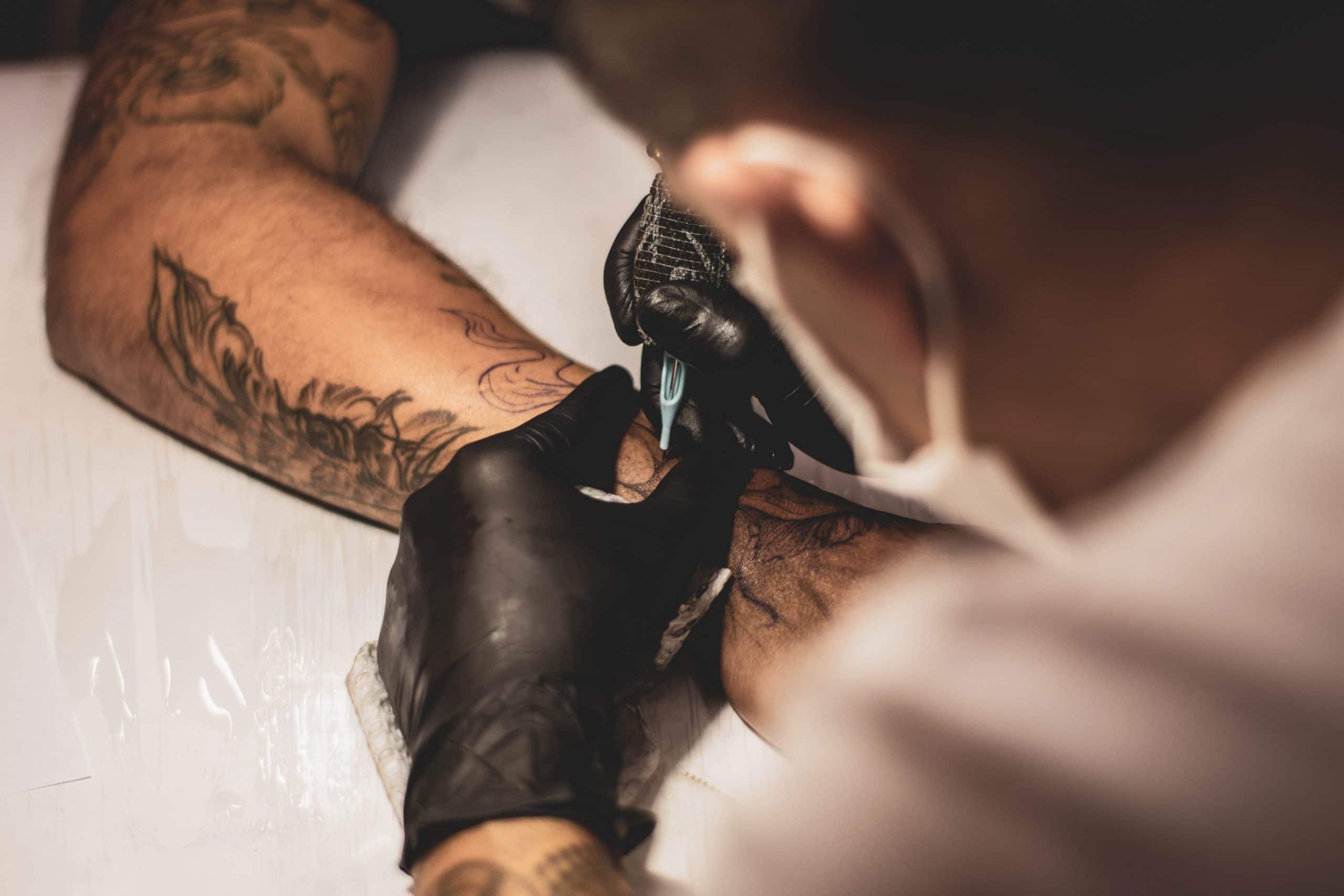 Tatoeëerder aan het werk. Hij houdt met één hand de hand van de klant vast en in de andere hand de tattoopen.